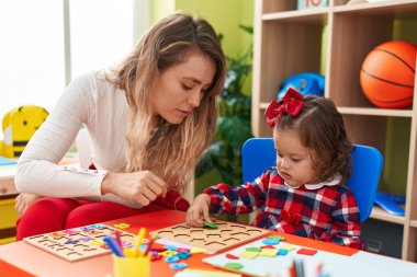 Teacher and toddler playing with maths puzzle game sitting on table at kindergarten
