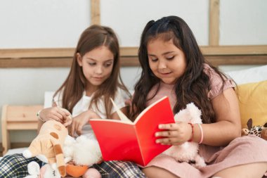 Two kids reading story book sitting on bed at bedroom