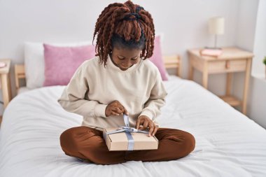 African american woman unpacking gift sitting on bed at bedroom