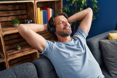 Orta yaşlı bir adam evdeki kanepede rahat bir şekilde müzik dinliyor.