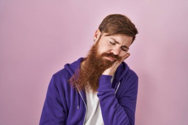 Caucasian man with long beard standing over pink background thinking looking tired and bored with depression problems with crossed arms. 