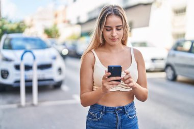 Sokakta akıllı telefon kullanan, kendine güvenen genç sarışın kadın.