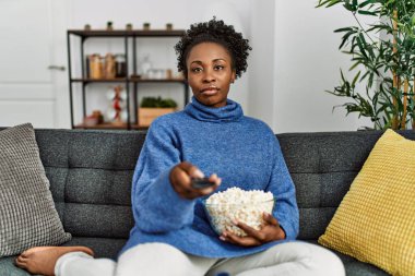 Afro-Amerikalı kadın evde kanepede oturmuş film izliyor.