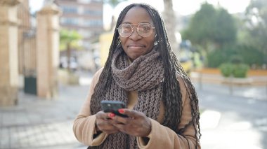African woman smiling using smartphone at street