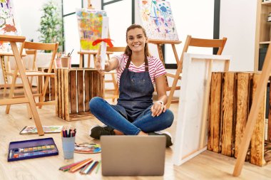 Sanat stüdyosunda kendine güvenen, gülümseyen genç bir kadın.