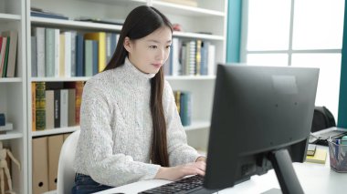 Young chinese woman student using computer studying at library university