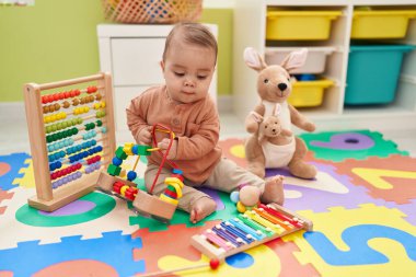 Sevimli İspanyol çocuk anaokulunda yerde oturmuş oyuncaklarla oynuyor.