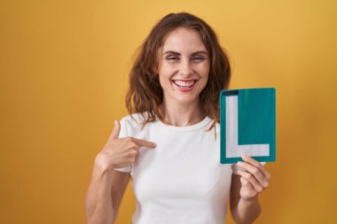 Beautiful brunette woman holding l sign for new driver pointing finger to one self smiling happy and proud 