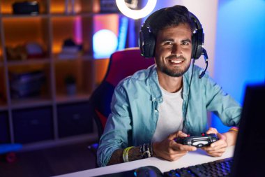 Young hispanic man streamer playing video game using joystick at gaming room