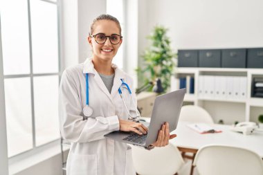 Klinikte çalışırken dizüstü bilgisayar kullanan doktor üniforması giyen genç sarışın kadın.