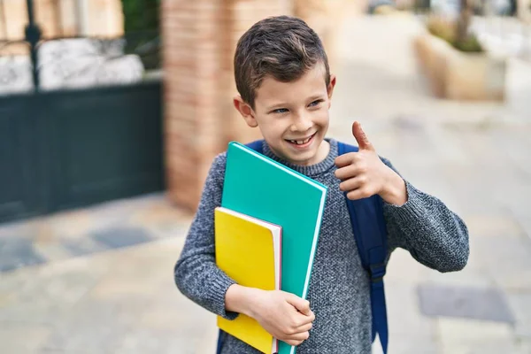 Blond child student holding books doing ok gesture at street