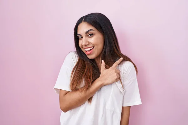 笑顔で明るいピンクの背景の上に立っている若いアラブ人女性は幸せと自然な表情で側に手と指で指しています — ストック写真