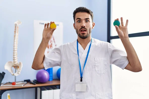 Young Hispanic Physiotherapist Man Holding Strength Balls Train Hand Muscles — Stockfoto