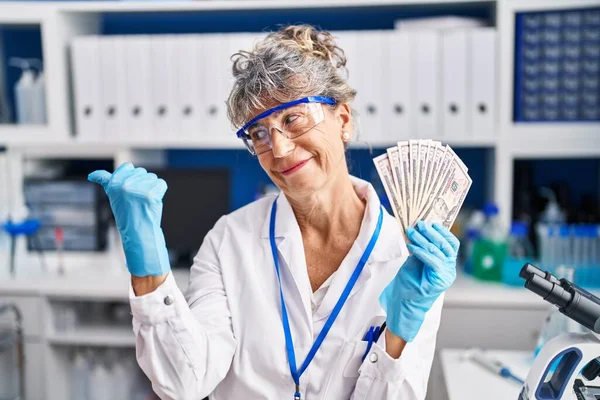 中年女性仕事で科学研究所保持ドル指差す親指へザサイド笑顔幸せとともにオープン口 — ストック写真