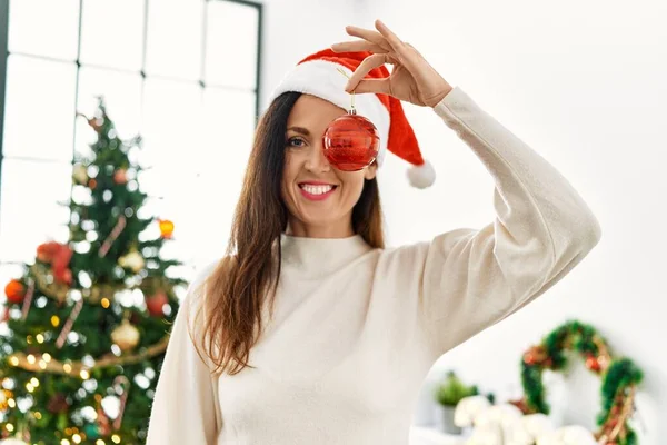 Middelbare Leeftijd Spaanse Vrouw Glimlachend Zelfverzekerd Houden Kerstbal Oog Thuis — Stockfoto