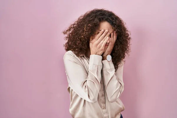Hispanic woman with curly hair standing over pink background rubbing eyes for fatigue and headache, sleepy and tired expression. vision problem