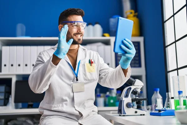 Young hispanic man wearing scientist uniform having video call at laboratory