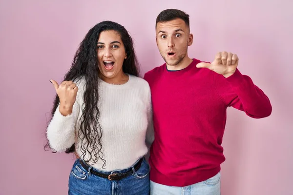Young Hispanic Couple Standing Pink Background Surprised Pointing Hand Finger — Fotografia de Stock