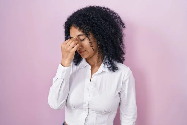 ピンクの背景に立っている巻き毛を持つヒスパニック系の女性は 鼻と目の疲労感や頭痛をこすり疲れている ストレスとフラストレーションの概念 — ストック写真