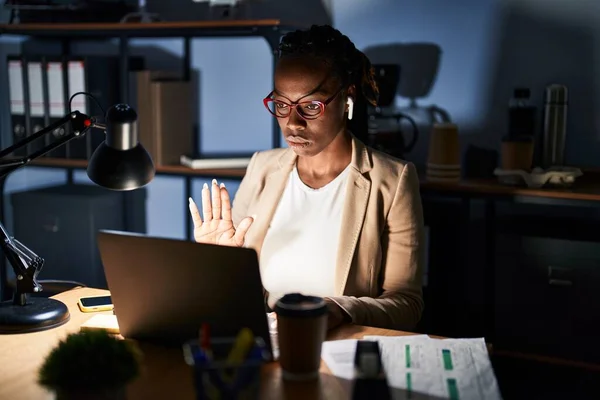 Beautiful black woman working at the office at night doing stop sing with palm of the hand. warning expression with negative and serious gesture on the face.