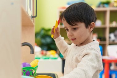 Adorable hispanic boy playing with play kitchen standing at kindergarten