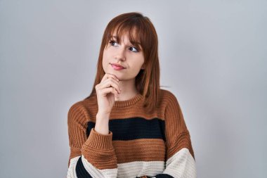 Young beautiful woman wearing striped sweater over isolated background with hand on chin thinking about question, pensive expression. smiling with thoughtful face. doubt concept. 