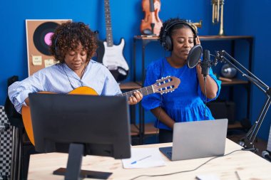 Afrikalı Amerikalı kadın müzisyenler müzik stüdyosunda klasik gitar çalarak şarkı söylüyorlar.