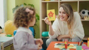 Teacher and toddler sitting on table having language lesson at kindergarten