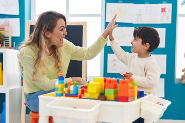 Teacher and toddler playing with construction blocks high five at kindergarten