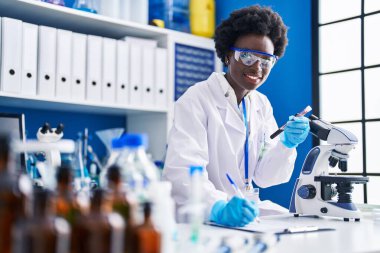 Young african american woman scientist writing on document holding blood analysis test tube at laboratory