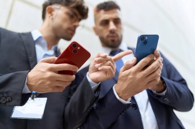 Two hispanic men business workers using smartphones at street