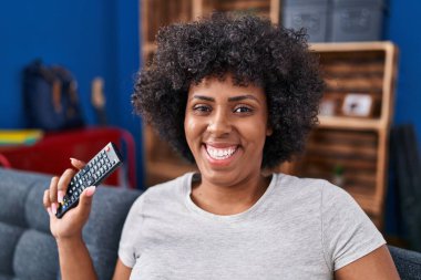 African american woman watching television holding television remote controller at home