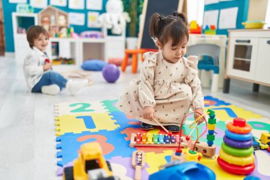 Two kids playing with dolls sitting on bed at kindergarten