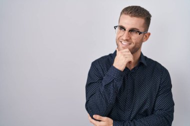 Young caucasian man standing over isolated background looking confident at the camera smiling with crossed arms and hand raised on chin. thinking positive. 