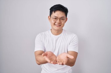 Young asian man standing over white background smiling with hands palms together receiving or giving gesture. hold and protection 