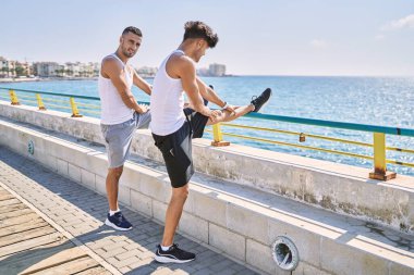 İki İspanyol erkek, deniz kenarında gerinerek gülümsüyor.