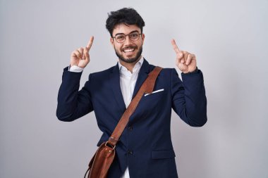 Hispanic man with beard wearing business clothes smiling amazed and surprised and pointing up with fingers and raised arms. 