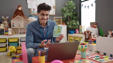Young hispanic man preschool teacher having online vocabulary lesson at kindergarten