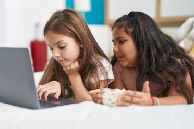 Two kids watching movie on laptop lying on bed at bedroom