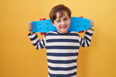 Sarı arka planda kaykay yapan beyaz bir çocuk kameraya seksi bir ifadeyle bakıyor, neşeli ve mutlu bir yüzle.. 