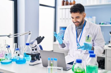Young hispanic man wearing scientist uniform having video call at laboratory