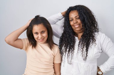 Anne ve küçük kızı beyaz arka planda durup gülümseyerek saçlarına dokunarak el hareketleriyle çekici ve modaya uygun bir poz veriyorlar. 