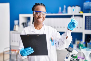 African american woman scientist holding test tube reading document at laboratory
