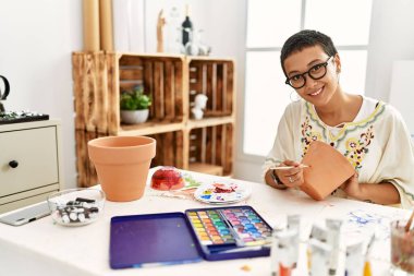 Sanat atölyesinde kilden seramik boyarken gülümseyen genç İspanyol kadın.