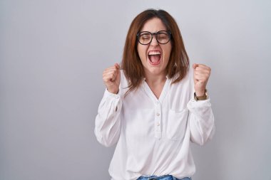 Brunette woman standing over white isolated background excited for success with arms raised and eyes closed celebrating victory smiling. winner concept. 