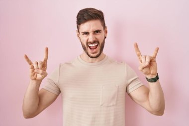 Hispanic man with beard standing over pink background shouting with crazy expression doing rock symbol with hands up. music star. heavy music concept. 