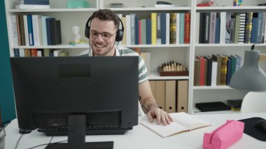 Young caucasian man using computer wearing headphones at library university