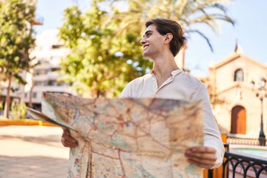 Young caucasian man smiling confident holding city map at park
