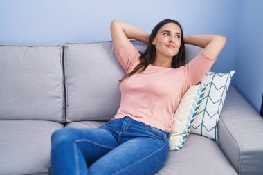 Genç, güzel, İspanyol bir kadın. Elleri başının üstünde, evdeki kanepede oturuyor.