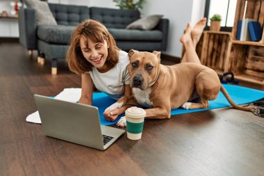 Beyaz kadın sporcu. Evde köpekli dizüstü bilgisayar kullanarak gülümsüyor.